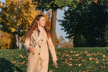 Happy trendy middle aged woman in beige coat outside in the city park in autumn. Woman joyfully walking while spending time in park. Fashion and good mood concept.