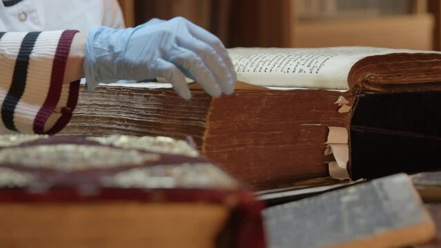 New museum old exhibit. Stock footage. Young specialists in gloves study Old Slavonic scriptures in a thick book.