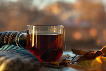 Tea bag and a cup of tea on the windowsill in autumn. Autumn dry leaves, a warm knitted scarf and hot tea create an autumn mood. Evening sunlight on the windowsill of the balcony.