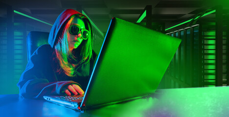 Woman programmer. Laptop on desk hacker girl. Female in hooded sunglasses. Programmer uses computer...