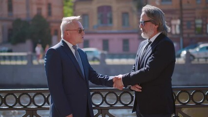 Two mature businessmen standing near river in city talking. Realtime