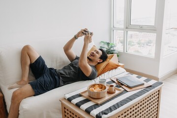 Lazy happy asian man playing mobile game while he should have work from home.