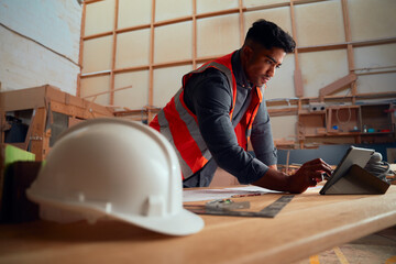 Young man writing with digitized pen on digital tablet next to safety helmet in woodworking factory