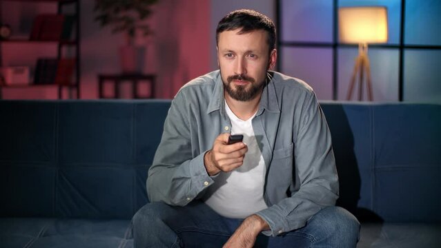 Pensive bearded guy surfing TV video channel thinking problem suffering loneliness at evening home
