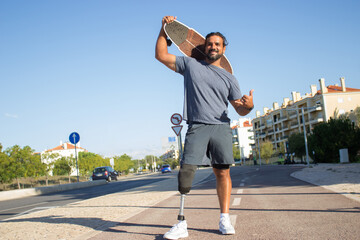 Portrait of carefree bearded man with skateboard. Mid adult sportsman in casual clothes and...