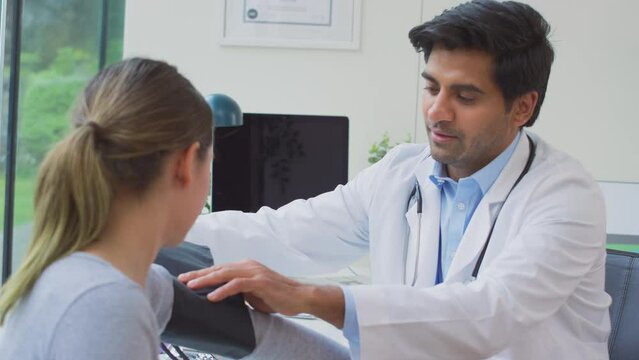 Male doctor or GP wearing white coat examining teenage girl taking blood pressure with sphygmomanometer - shot in slow motion