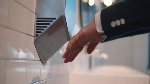 Cropped shot of man in suit using hand dryer in public bathroom. Realtime