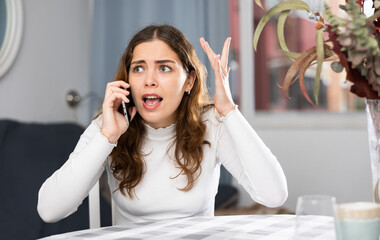 Angry caucasian woman arguing while having telephone conversation at home.