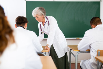 Experienced elderly female professor of medicine giving lecture to group of young adult students at...