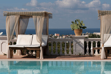 Crete, Greece.2022. Sunbeds with drapes and mattress for two siuated around a swimming pool