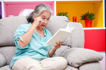 Asian elderly woman Sitting on the sofa in the house reading a book. The concept of life of the elderly in retirement age. health care