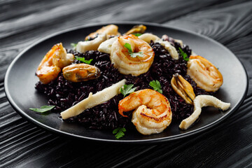 delicious black rice with shrimps and seafood on a black wooden rustic background