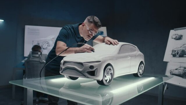 Automotive engineer makes the design corrections to a prototype car sculpture. Perfecting it using the milling machine. A high tech laboratory with LED and sketches of a new car model.