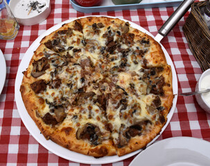 Pizza on a table with red checkered tablecloth in  a restaurant.