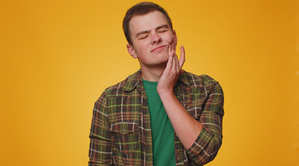 Teenager young man touching sore cheek suffering from toothache cavities or gingivitis waiting for dentist appointment, gums disease. Adult boy indoors studio shot isolated alone on yellow background