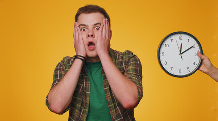 Confused young man with anxiety checking time on clock, running late to work, being in delay, deadline on yellow studio background. Serious boy looking at hour and minutes, worrying to be punctual