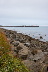 View of the pier in the sea bay. Motor boats near the pier. Rocky coast. Autumn seascape. Overcast weather. Gertner Bay, Sea of Okhotsk, Magadan Region, Russian Far East.