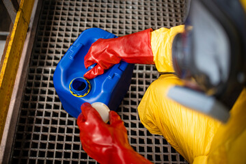 Worker in yellow protection suit and gas mask opening canister with chemicals inside factory.