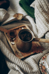 black coffee in coffee turk in knitted beige sweater on rumpled bed, top view, monochrome cozy picture of Breakfast, vertically, selective focus