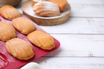 Delicious madeleine cookies and baking mold on white wooden table, closeup. Space for text