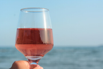 Woman holding glass of tasty rose wine near sea, closeup. Space for text