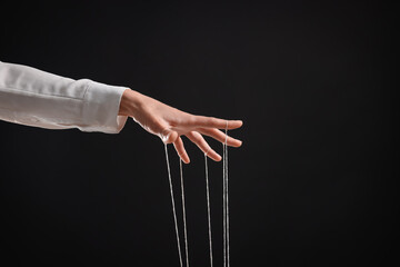 Woman pulling strings of puppet on black background, closeup. Space for text