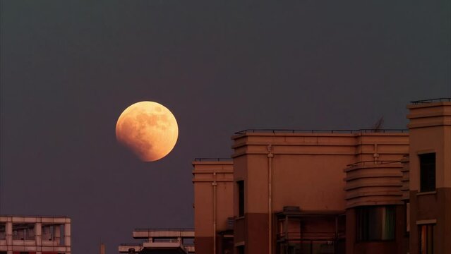 4k time lapse footage of yellow super moon moving up in sky with residential buildings foreground from evening to night, lunar eclipse timelapse video.
