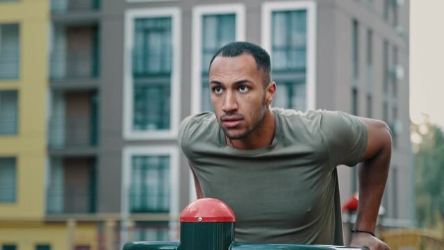 Male professional bodybuilder strong african latina ethnic man sportsman male athlete in good physical shape push ups on parallel bars performing sport exercises on city sports ground healthy workout