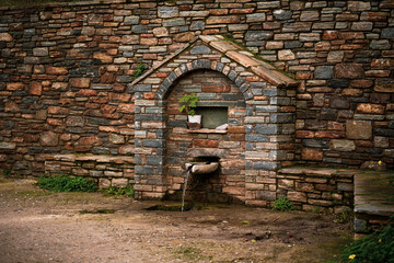 Old beautiful well in a stone wall. Countryside of Greece.