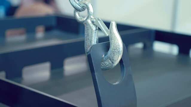 New shiny metal hook on a cable with a safety clamp, hooked on a metal structure and yellow winch remote control with raise, lower and emergency red button. Shot in motion. Closeup