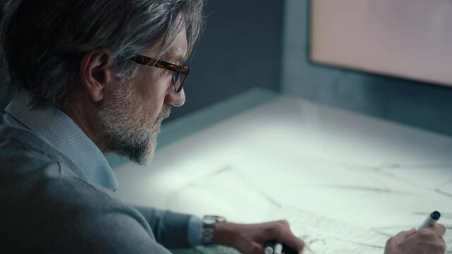 Senior automotive graphic designer with black framed glasses and beard works in a high tech innovative laboratory. Draws sketch of the prototype model of a car render.