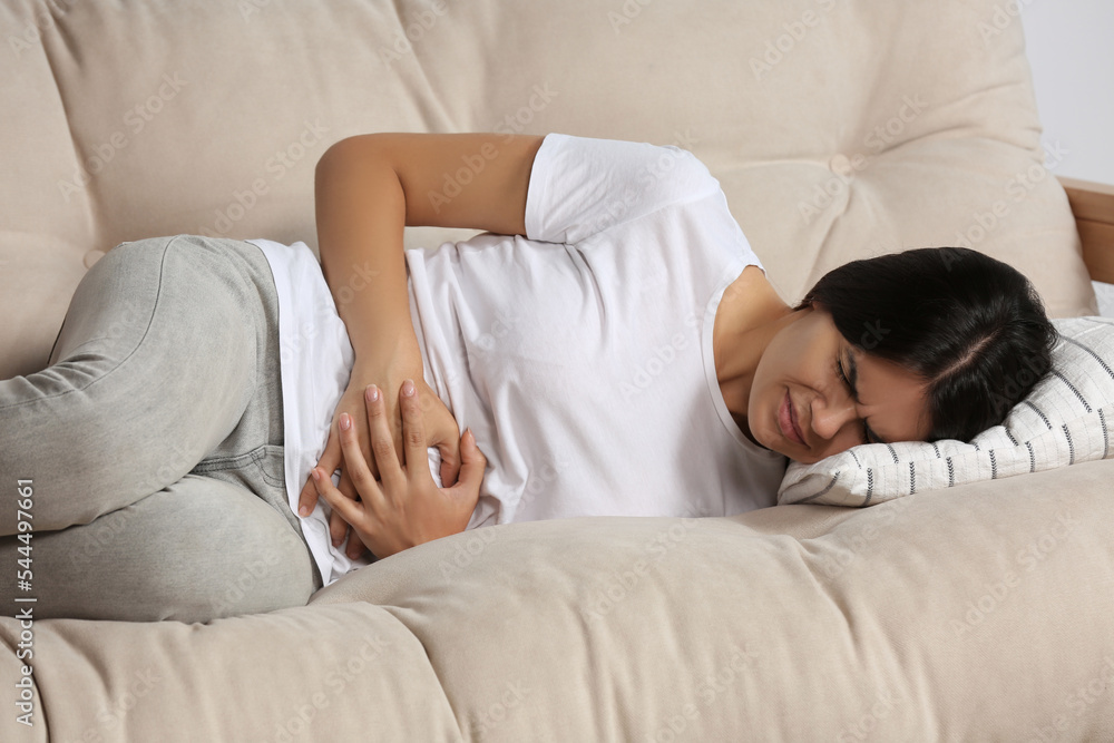 Sticker Young woman suffering from menstrual pain on sofa indoors