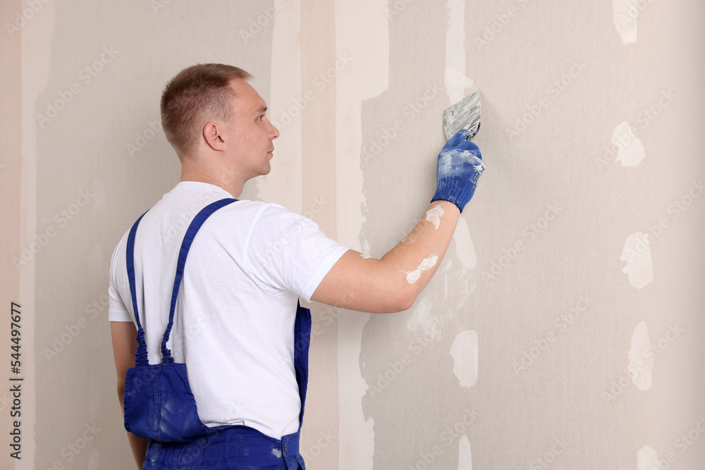 Poster Man plastering wall with putty knife indoors. Home renovation