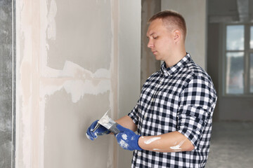 Worker with putty knives and plaster near wall indoors. Home renovation