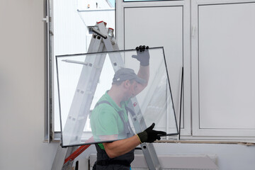 Worker near folding ladder installing window indoors