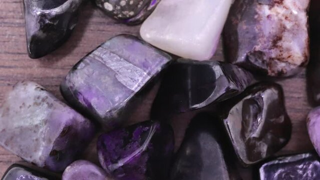 Sugilite rare jewel stones on brown varnished wood texture. Moving right seamless loop backdrop.