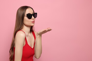 Beautiful young woman with sunglasses blowing kiss on pink background, space for text © New Africa