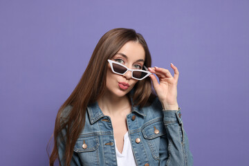 Naklejka premium Beautiful young woman with sunglasses blowing kiss on purple background