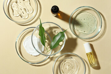 Petri dishes with cosmetic products and leaves on beige background, flat lay