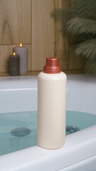 Beige bottle of bubble bath and candles on tub indoors