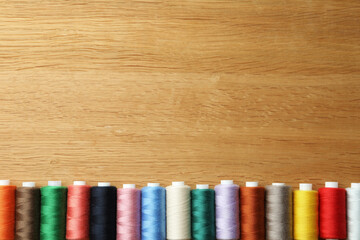 Many colorful sewing threads on wooden table, flat lay. Space for text