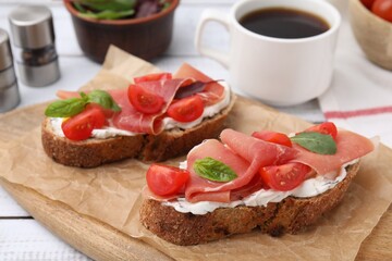 Tasty bruschettas with prosciutto, tomatoes and cheese on white wooden table