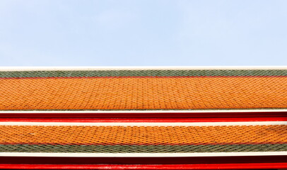 Ancient style of ceramic tile roof pattern and light blue sky. Green, red, orange color row of tiles on rooftop in temple, Thailand.