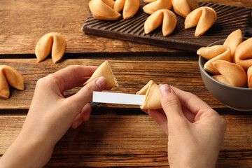Woman holding tasty fortune cookie with prediction at wooden table, closeup. Space for text