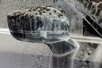 Naklejka na ściany i meble Automobile side-view mirror with cleaning foam at car wash, closeup