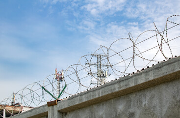 view of a high concrete fence with barbed wire at the top against the blue sky and telecommunication towers for radio communication