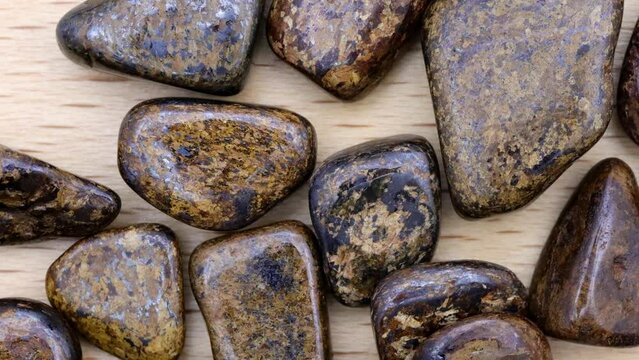 Bronzite heap up jewel stones texture on light varnished wood background. Moving right seamless loop backdrop.