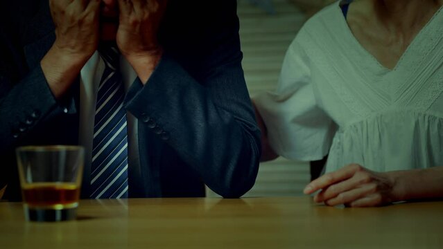 家でうなだれるミドル男性と彼を慰めるミドル女性