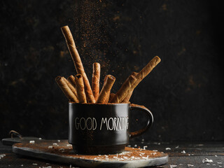 Cozy home composition. Fragrant cinnamon sticks in a black cup on a dark background. Spices,...