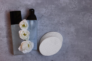 Luxury cosmetic products with flowers and cotton pads on grey table, flat lay. Space for text